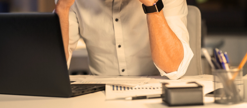 A man sitting with his head in his hands with loads of paperwork in front on a desk