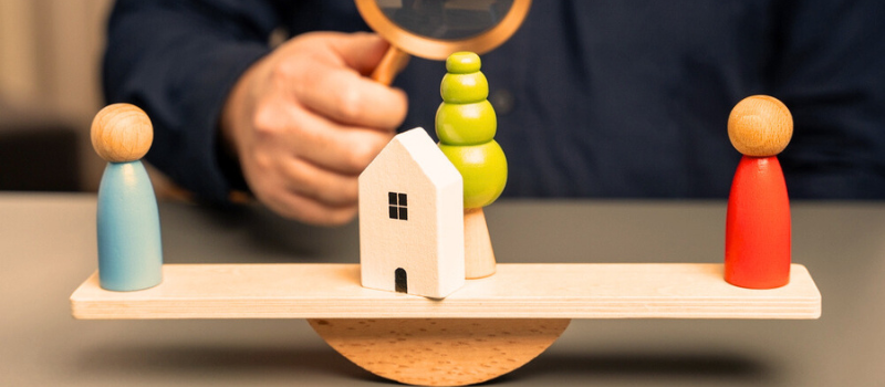 wooden swing with two figures at each end with a house in between