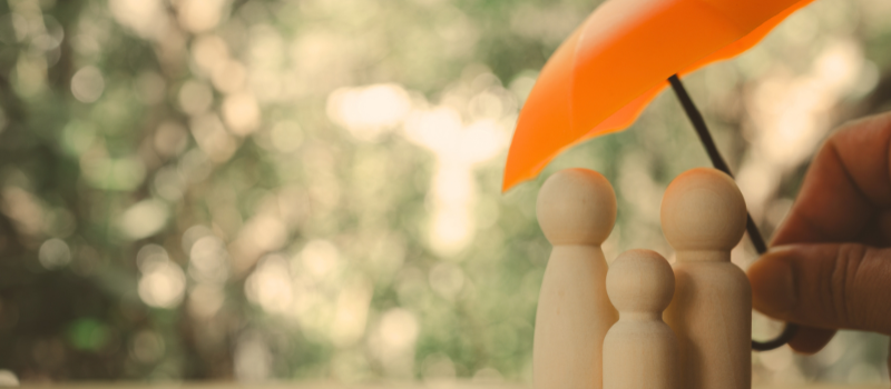 3 wooden figurines with an orange umbrella above them