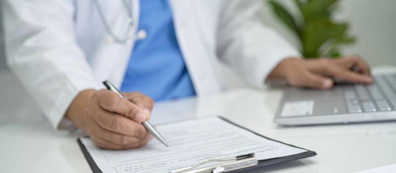 Medical professional sitting at a table with paperwork and computer