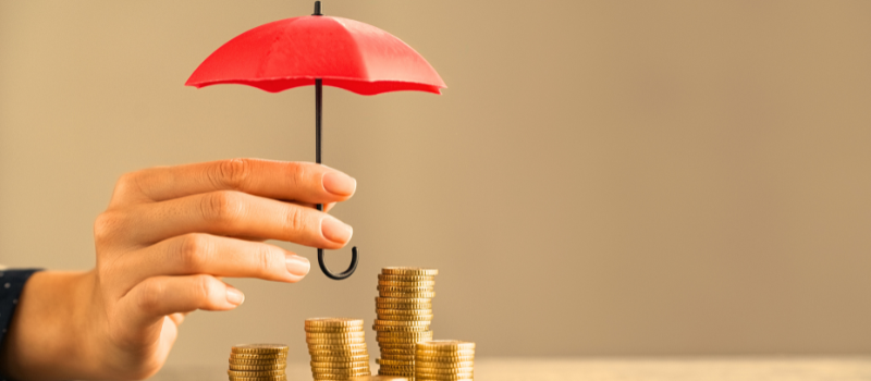 Hand holding an umbrella above coins