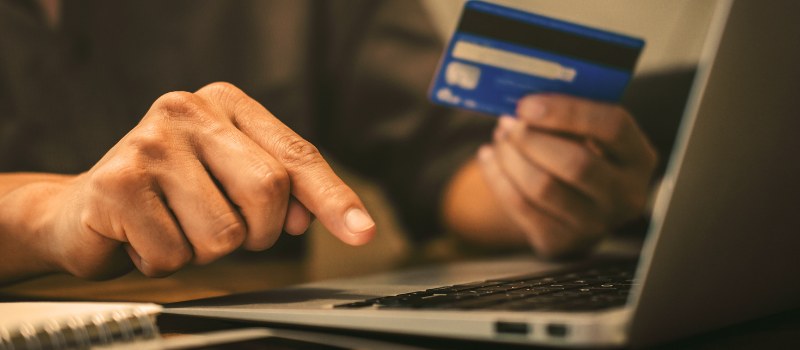 Persons hands with one about to click on a keyboard on an laptop and other holding a blue bank card